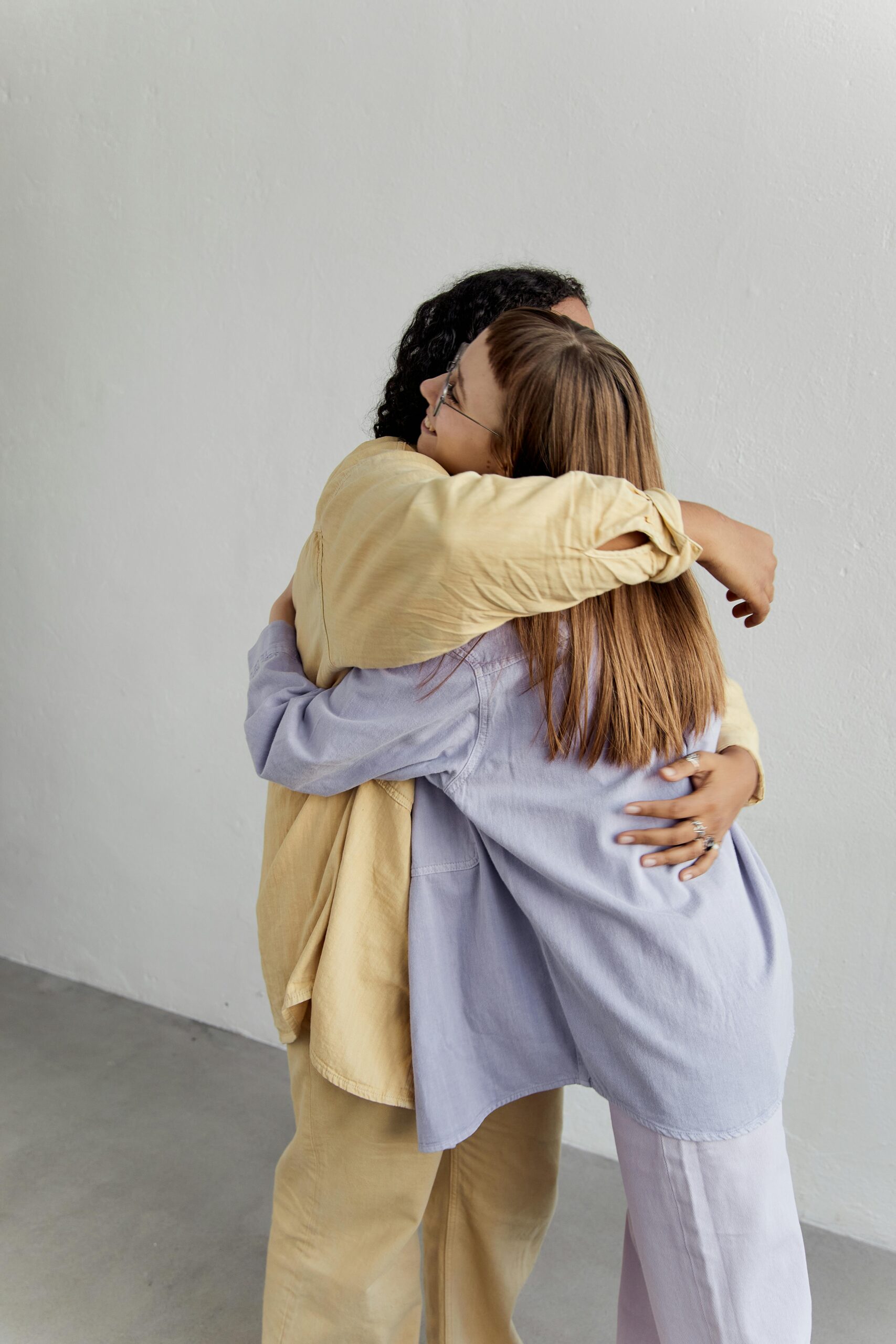 Two diverse women hugging warmly against a white background, expressing friendship and affection.